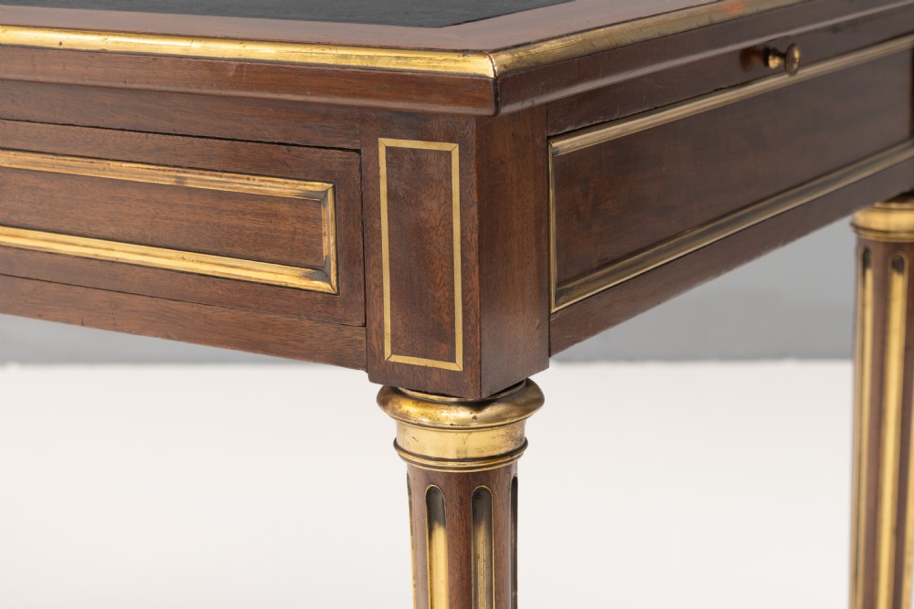 A French Louis XVI style mahogany bureau plat featuring a dark leather writing insert, gilt-bronze trim, frieze drawers, and fluted tapered legs. View VII