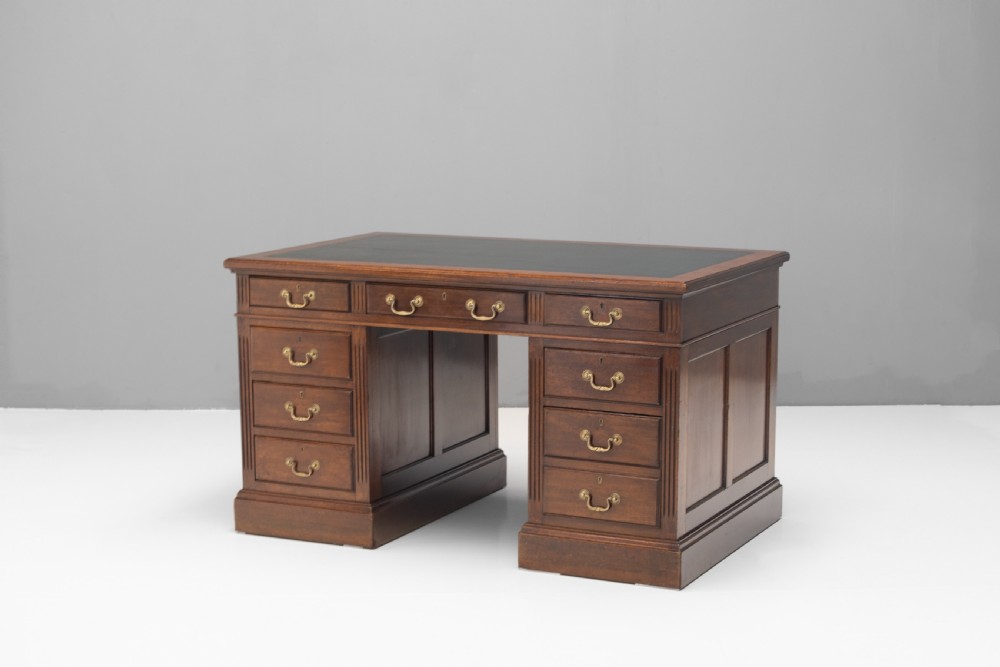 An antique mahogany pedestal desk featuring a dark leather top, fluted side columns, nine drawers with brass handles, and a central kneehole. View III