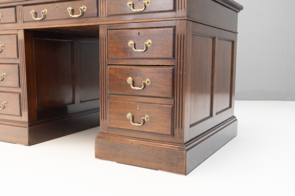 An antique mahogany pedestal desk featuring a dark leather top, fluted side columns, nine drawers with brass handles, and a central kneehole. View VIII
