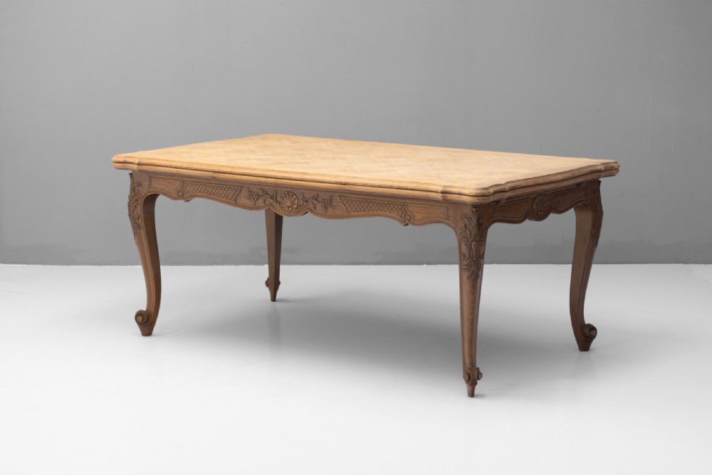 An extendable French Provincial oak dining table with a parquet top, carved shell apron, and cabriole legs ending in scroll feet.