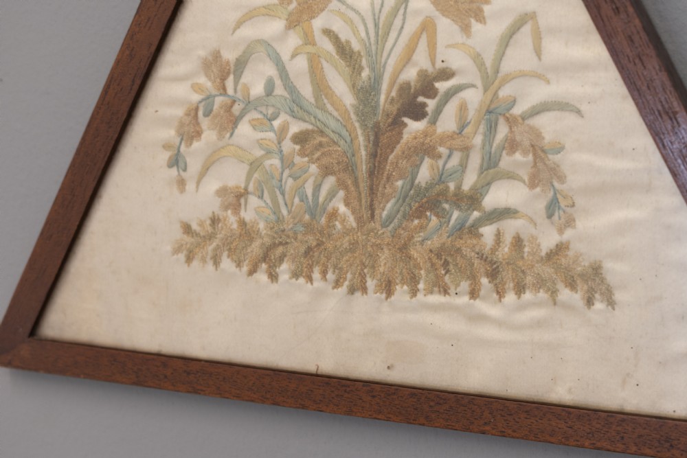 A pair of triangular wooden frames displaying hand-stitched botanical embroidery featuring floral motifs on a cream fabric ground. View IV