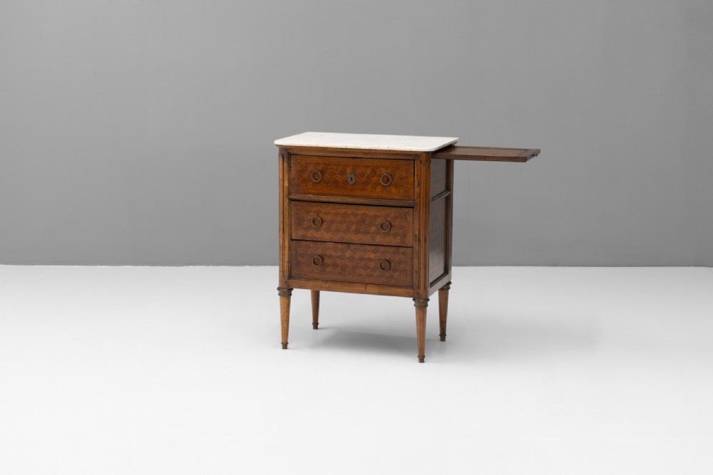 A Neoclassical style three-drawer wooden chest featuring geometric parquetry inlay, brass ring handles, tapered legs, and a white marble top surface. View II