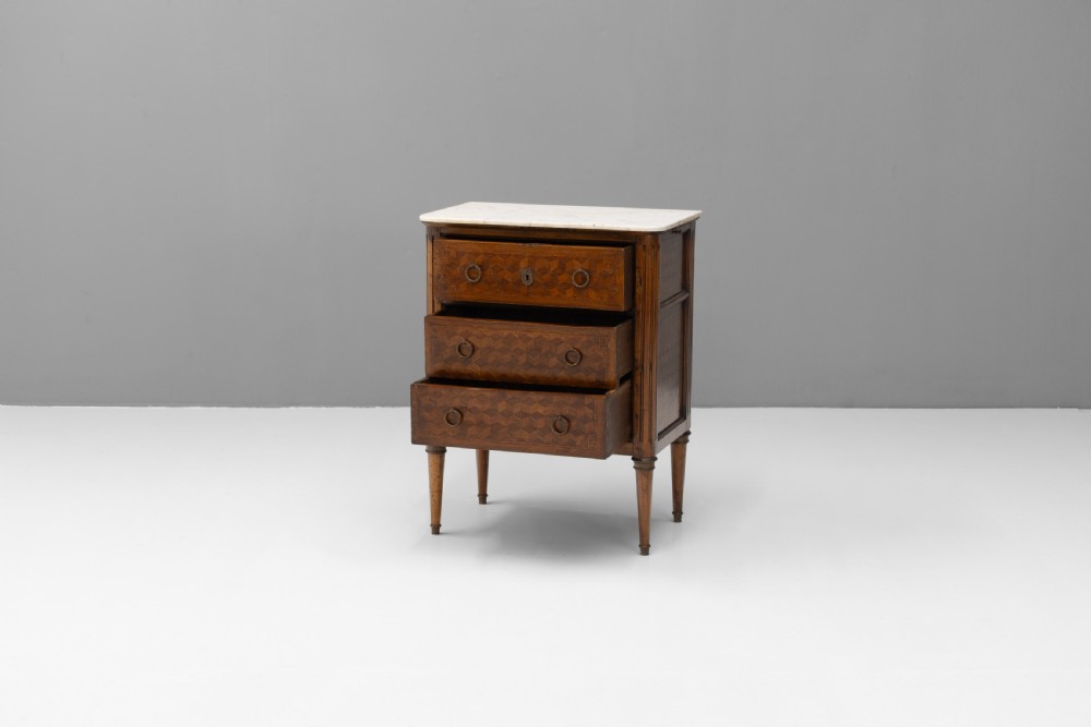 A Neoclassical style three-drawer wooden chest featuring geometric parquetry inlay, brass ring handles, tapered legs, and a white marble top surface. View III