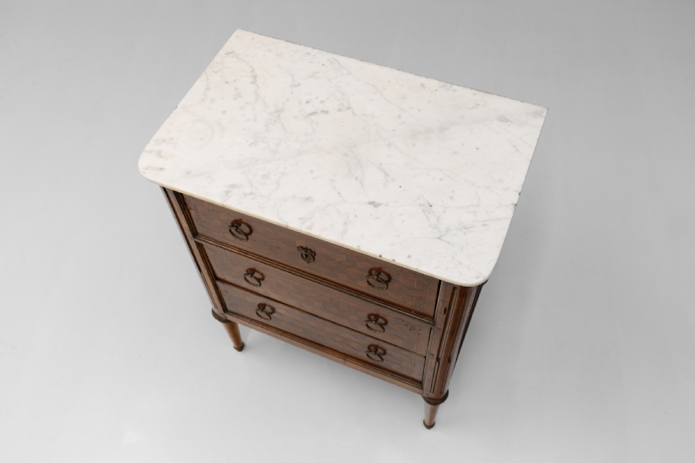 A Neoclassical style three-drawer wooden chest featuring geometric parquetry inlay, brass ring handles, tapered legs, and a white marble top surface. View V