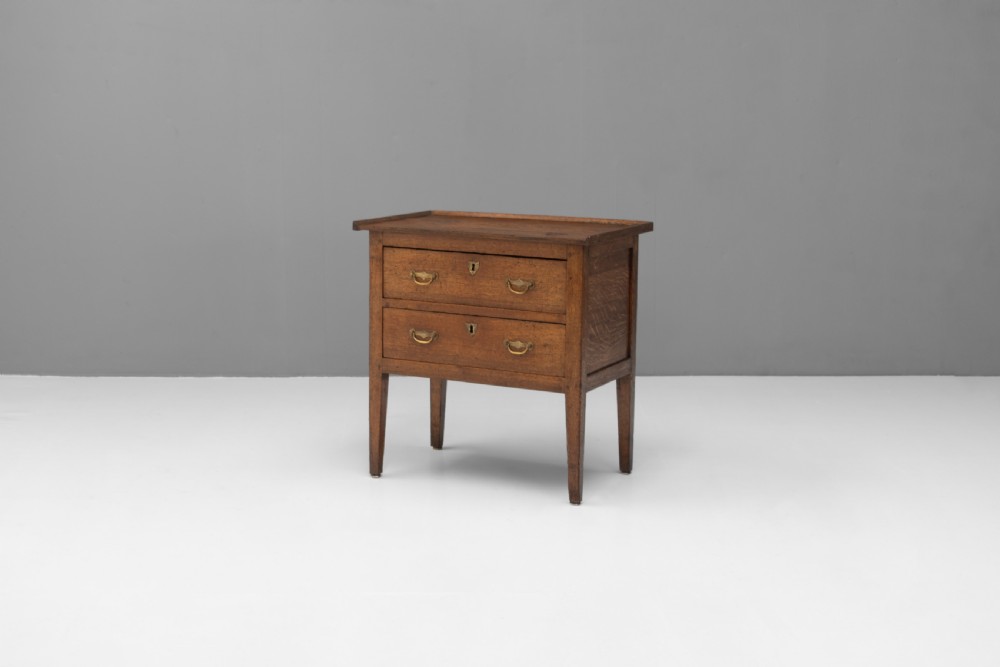 A Georgian oak two-drawer chest featuring brass drop handles, keyhole escutcheons, and square tapered legs against a neutral background.