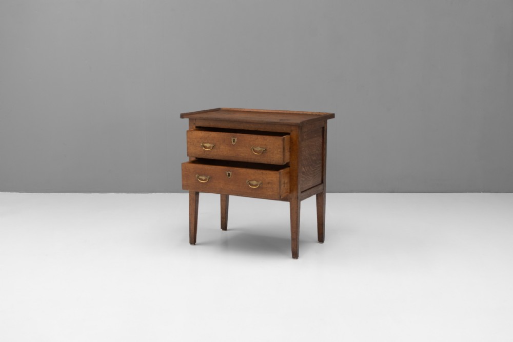 A Georgian oak two-drawer chest featuring brass drop handles, keyhole escutcheons, and square tapered legs against a neutral background. View II