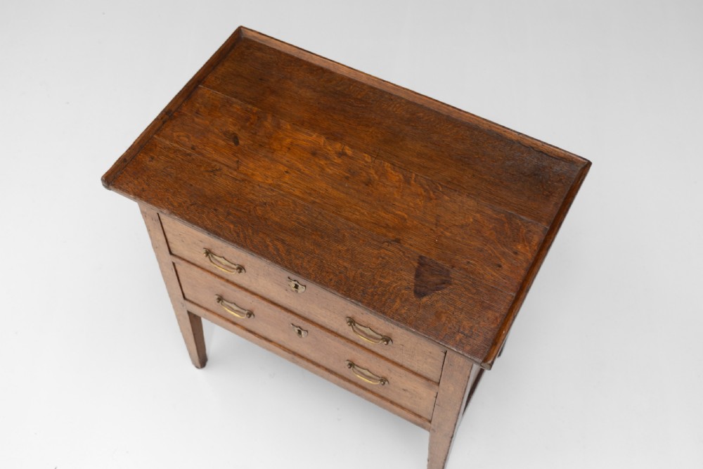 A Georgian oak two-drawer chest featuring brass drop handles, keyhole escutcheons, and square tapered legs against a neutral background. View IV