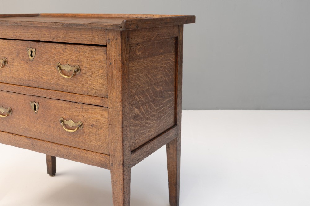 A Georgian oak two-drawer chest featuring brass drop handles, keyhole escutcheons, and square tapered legs against a neutral background. View VII