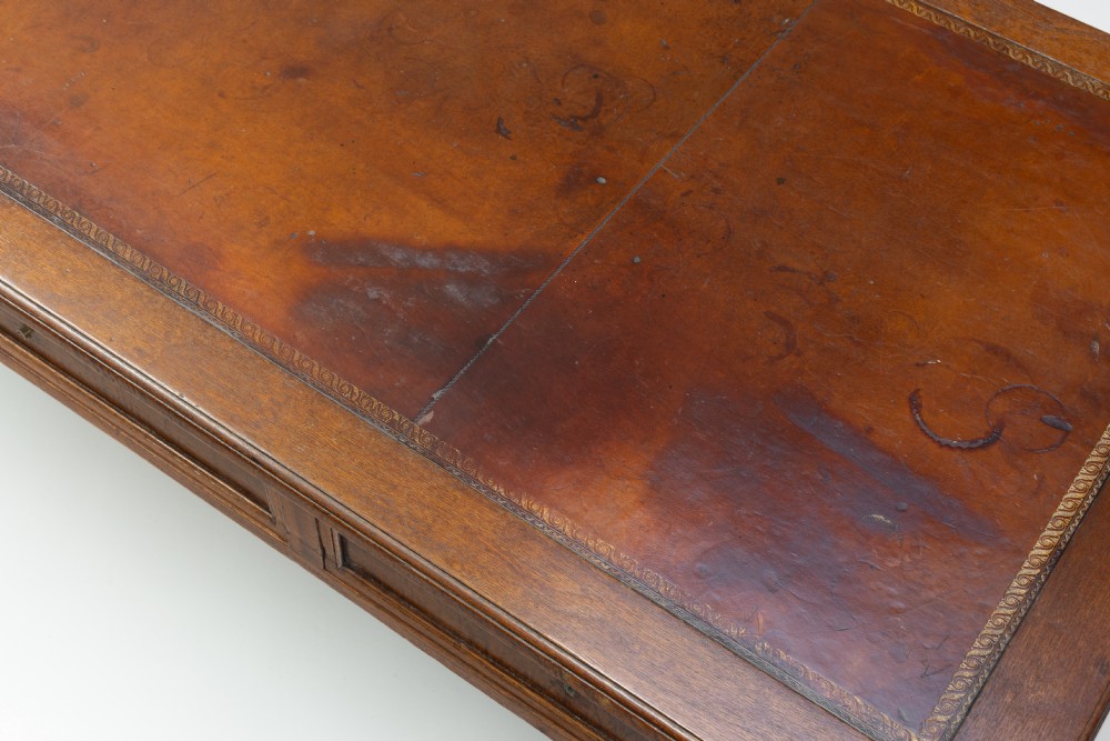 A rectangular mahogany writing table with an inset brown leather top, three frieze drawers, and four square tapered legs ending in brass caps. View VI