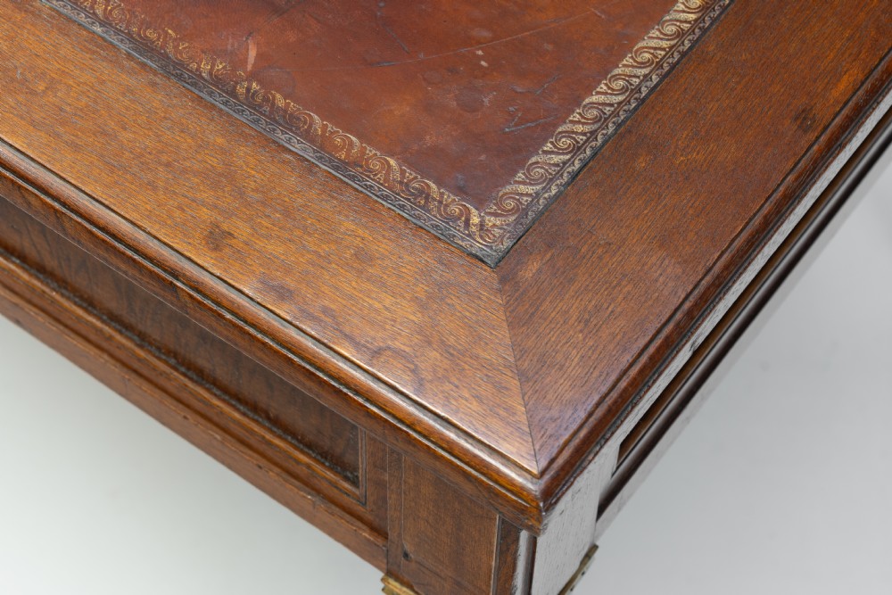 A rectangular mahogany writing table with an inset brown leather top, three frieze drawers, and four square tapered legs ending in brass caps. View VII