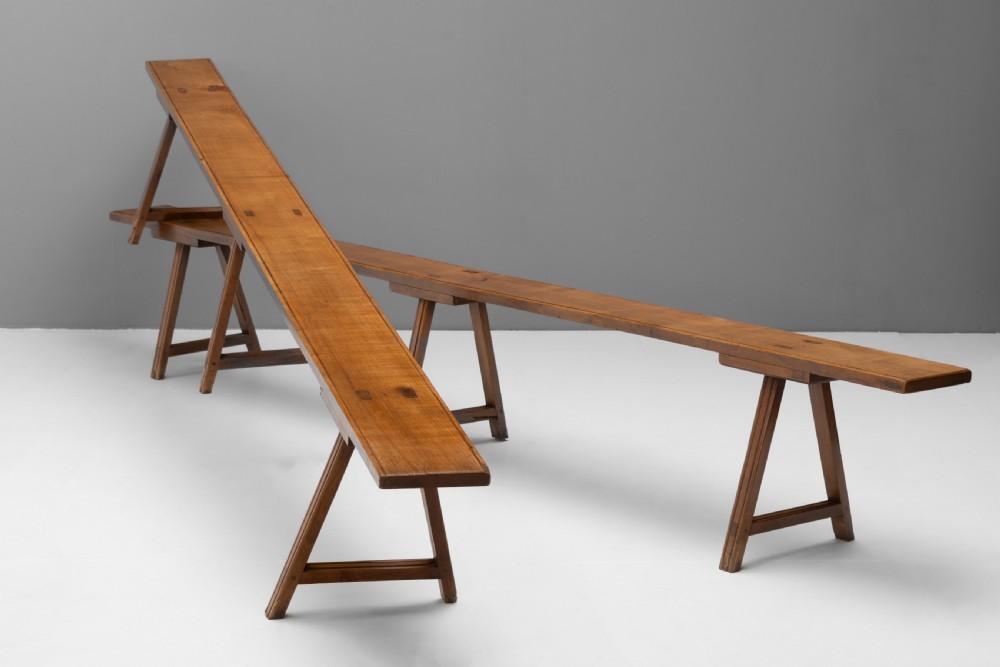 A pair of long cherry wood benches with narrow plank tops resting on angled trestle legs.