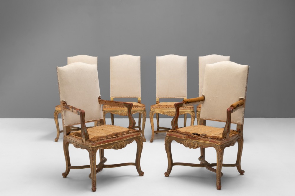 A set of six French gilded dining chairs featuring carved wooden frames, high backrests, and curved cabriole legs.