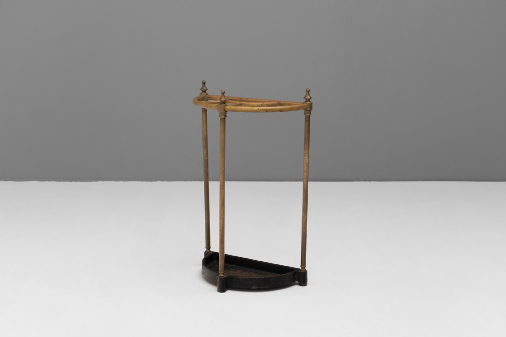 A semi-circular brass stick stand featuring tubular uprights topped with turned finials and supported by a heavy black cast iron drip tray base.