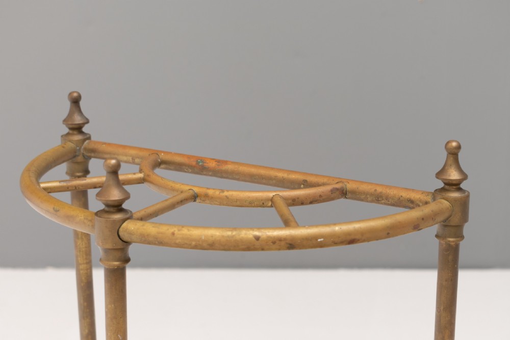 A semi-circular brass stick stand featuring tubular uprights topped with turned finials and supported by a heavy black cast iron drip tray base. View II