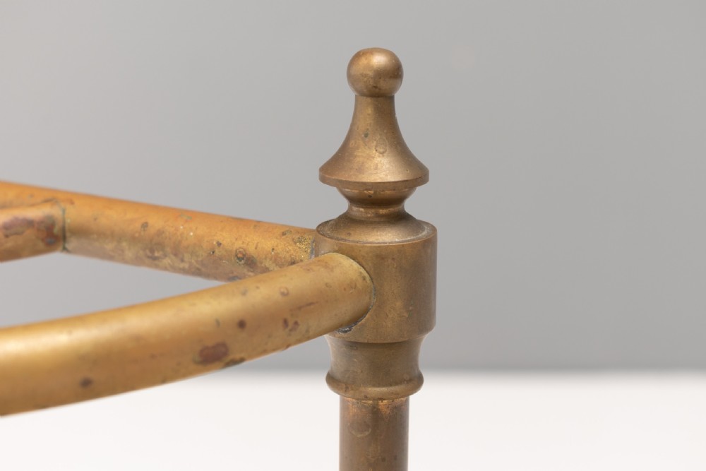 A semi-circular brass stick stand featuring tubular uprights topped with turned finials and supported by a heavy black cast iron drip tray base. View III