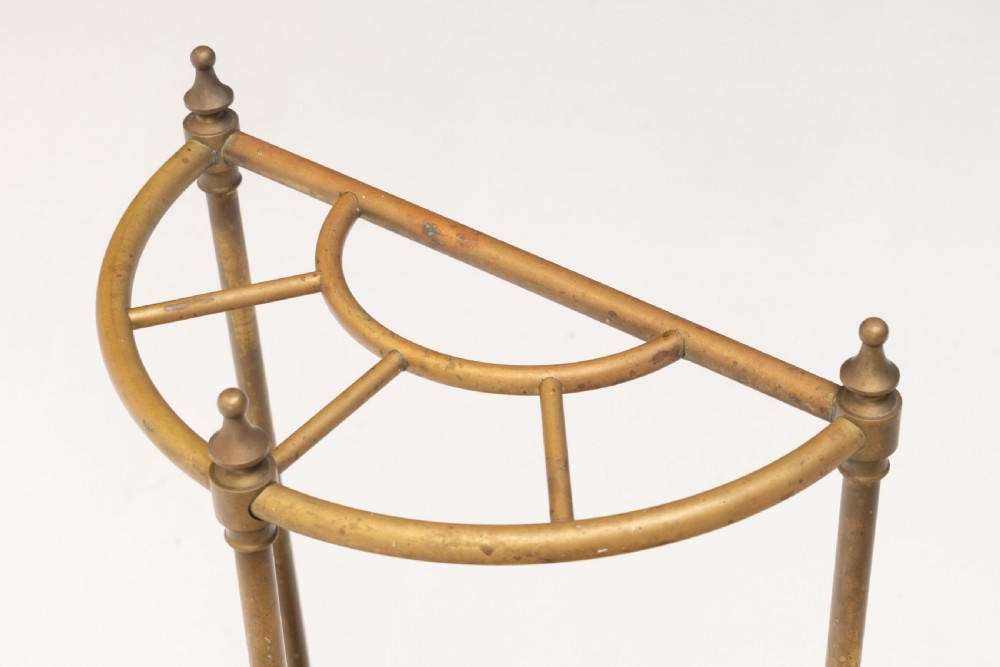 A semi-circular brass stick stand featuring tubular uprights topped with turned finials and supported by a heavy black cast iron drip tray base. View IV