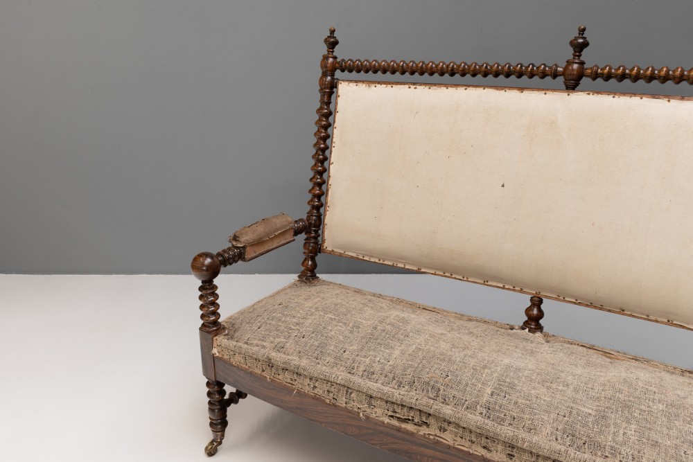 A 19th-century French bobbin-turned oak settee featuring a high upholstered back panel, spool-turned wooden framing, and brass castors. View II