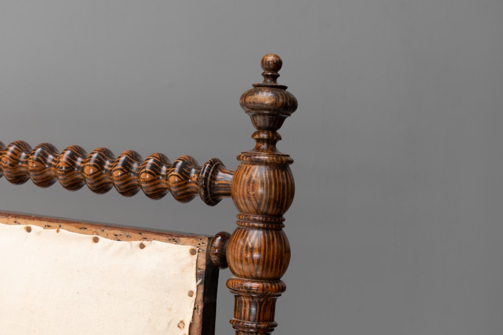A 19th-century French bobbin-turned oak settee featuring a high upholstered back panel, spool-turned wooden framing, and brass castors. View III