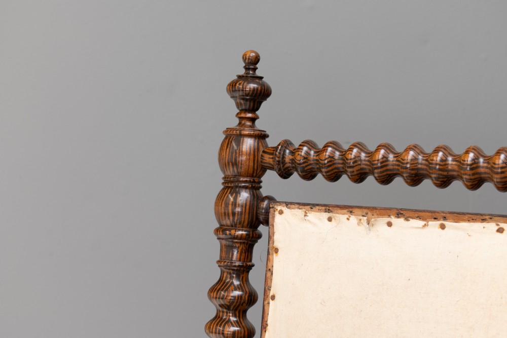 A 19th-century French bobbin-turned oak settee featuring a high upholstered back panel, spool-turned wooden framing, and brass castors. View IV