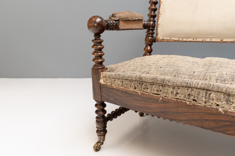 A 19th-century French bobbin-turned oak settee featuring a high upholstered back panel, spool-turned wooden framing, and brass castors. View V