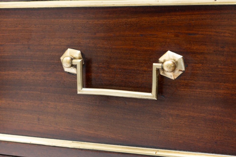 A dark mahogany French Louis XVI style chest of drawers featuring a grey marble top, brass linear moulding, brass swing handles, and turned tapered legs. View VII