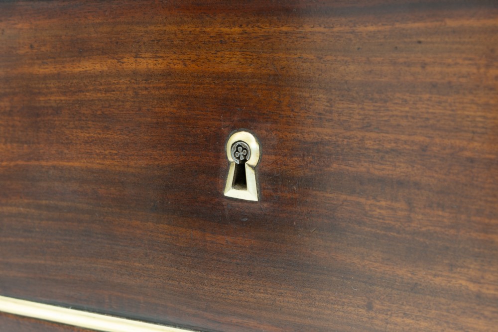 A dark mahogany French Louis XVI style chest of drawers featuring a grey marble top, brass linear moulding, brass swing handles, and turned tapered legs. View VIII