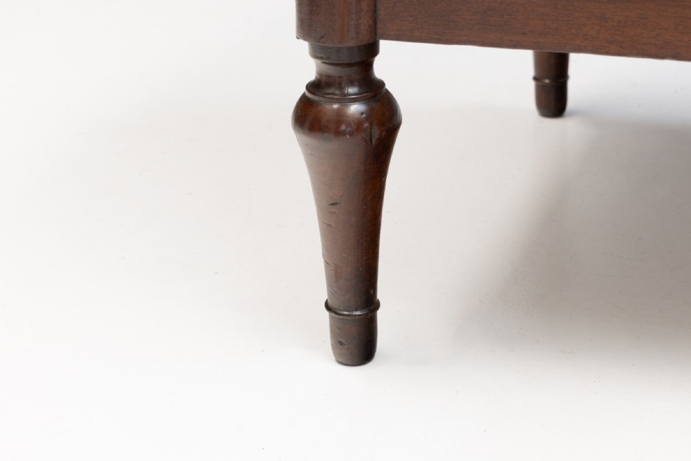 A dark mahogany French Louis XVI style chest of drawers featuring a grey marble top, brass linear moulding, brass swing handles, and turned tapered legs. View IX