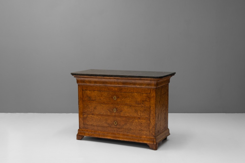 A 19th-century elm commode chest of drawers featuring a dark marble top, three full-width drawers with oval brass escutcheons, and a prominent figured wood grain.