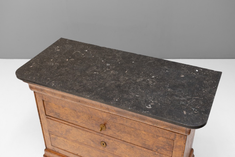 A 19th-century elm commode chest of drawers featuring a dark marble top, three full-width drawers with oval brass escutcheons, and a prominent figured wood grain. View IV
