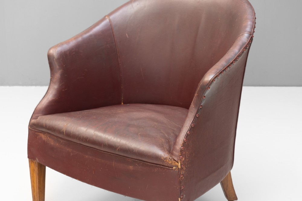 An antique dark brown leather tub chair featuring a rounded backrest, brass studding along the trim, and tapered timber legs on metal castors. View III