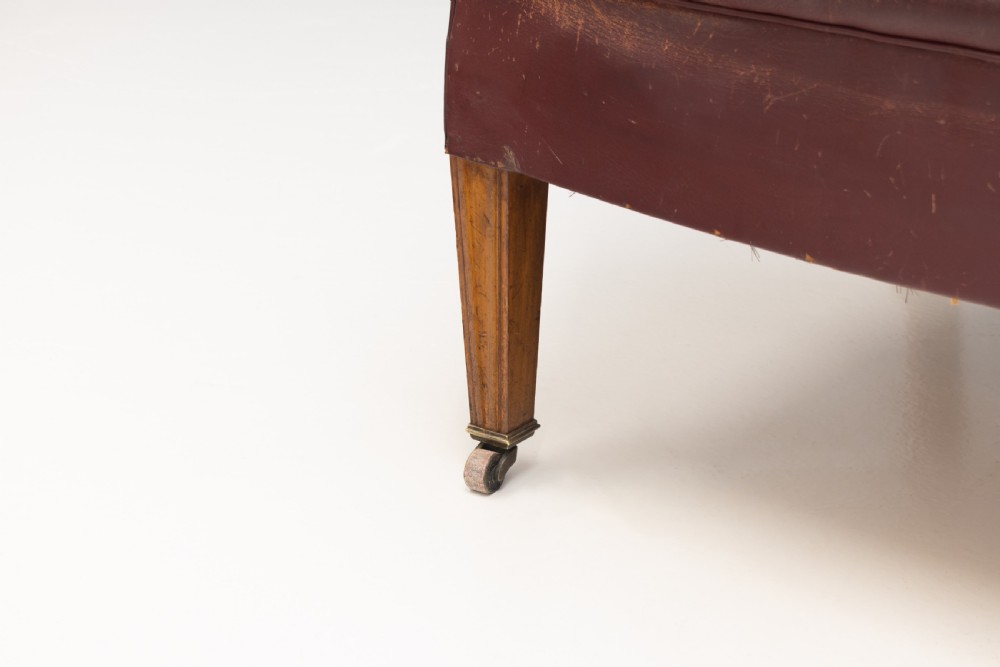 An antique dark brown leather tub chair featuring a rounded backrest, brass studding along the trim, and tapered timber legs on metal castors. View IV