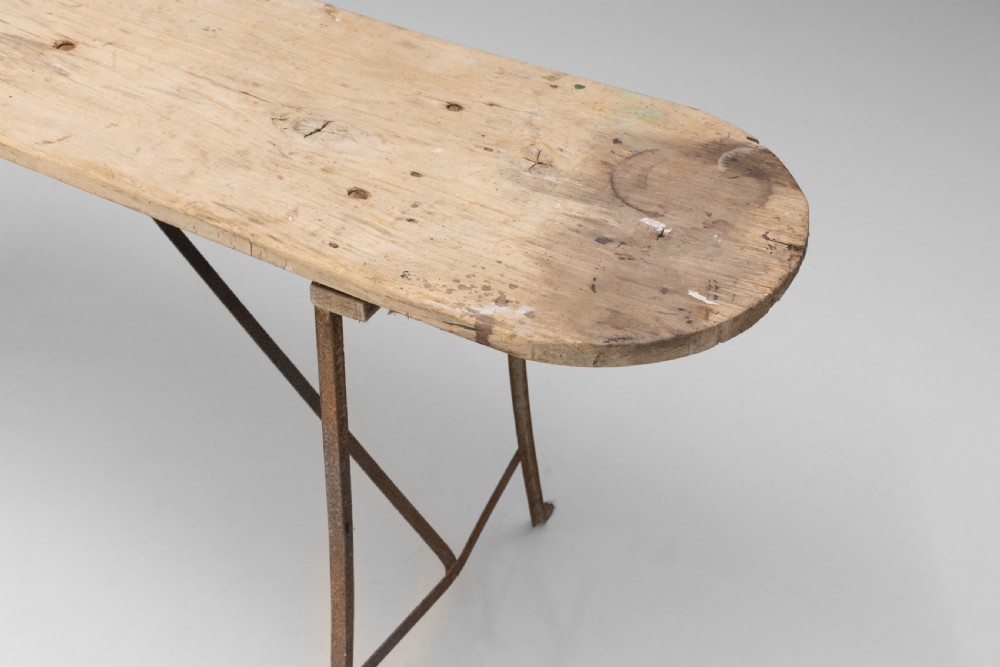 A long narrow rustic table featuring a natural pale wood top with rounded ends supported by slender brown metal legs with diagonal cross-bracing. View IV