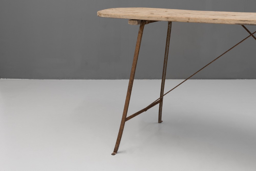 A long narrow rustic table featuring a natural pale wood top with rounded ends supported by slender brown metal legs with diagonal cross-bracing. View V