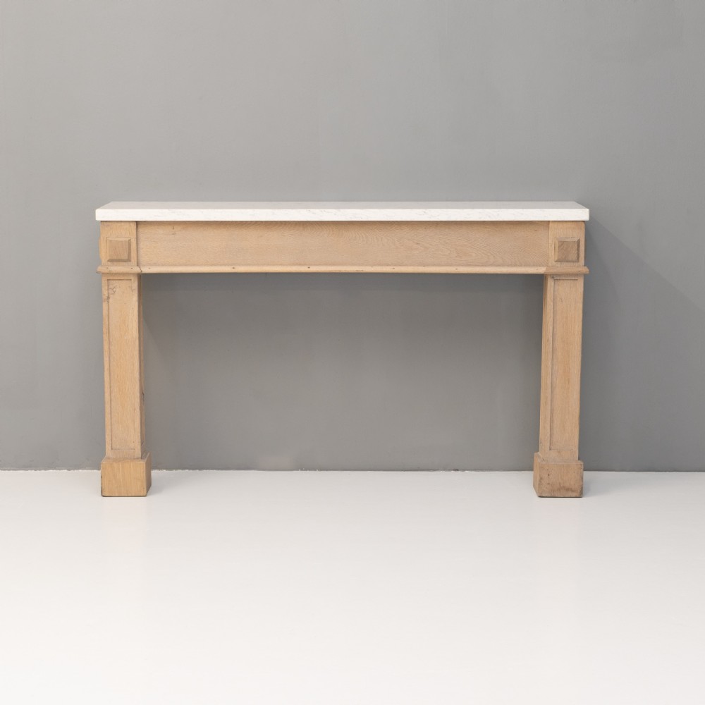 A light oak console table featuring rectangular pilaster legs on plinths and a thick rectangular white marble top set against a neutral grey wall.