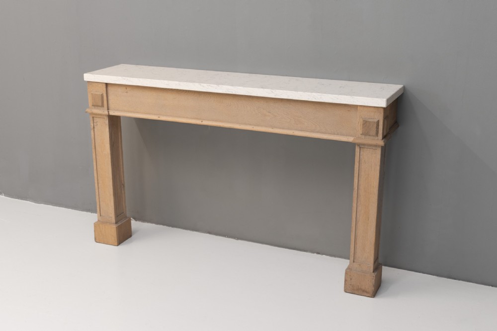 A light oak console table featuring rectangular pilaster legs on plinths and a thick rectangular white marble top set against a neutral grey wall. View IV