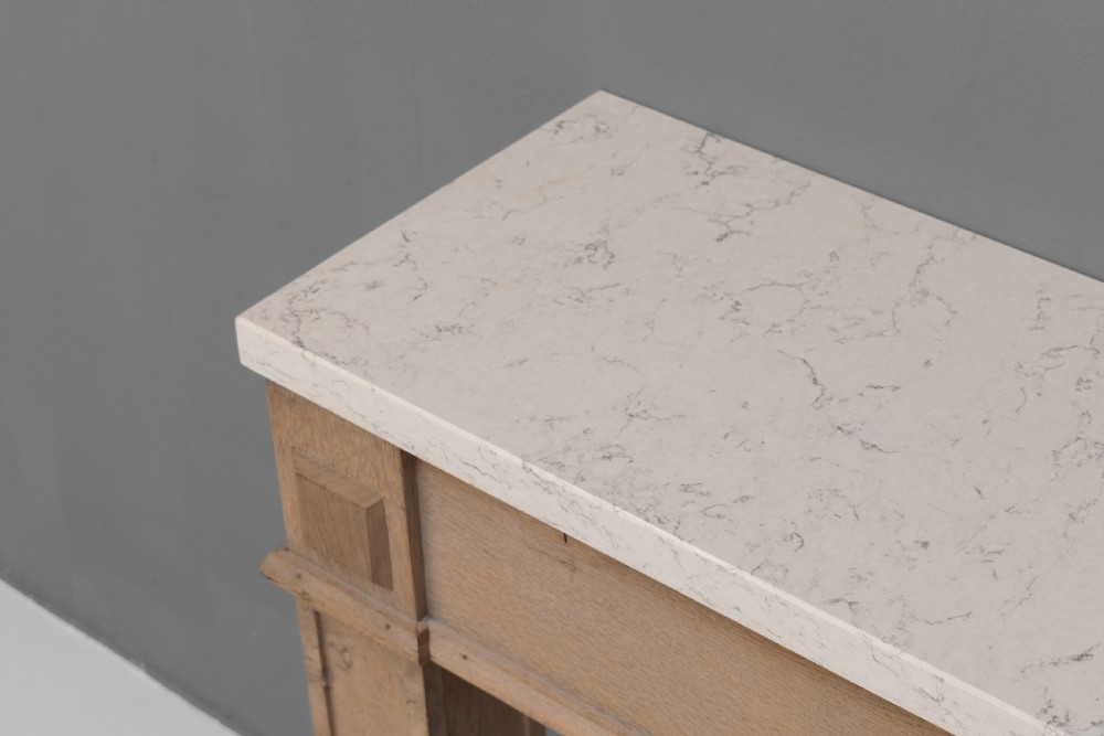 A light oak console table featuring rectangular pilaster legs on plinths and a thick rectangular white marble top set against a neutral grey wall. View VII