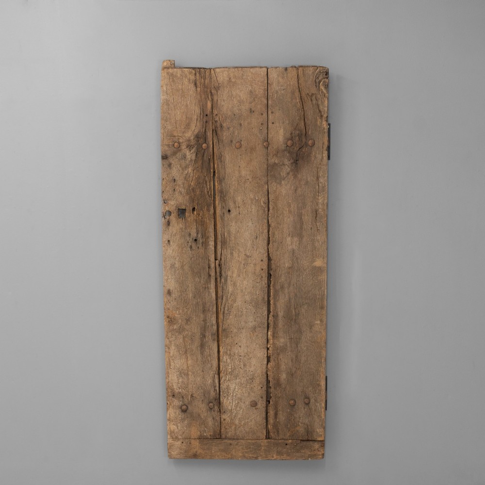 A tall weathered antique oak plank door featuring vertical wooden boards joined with visible iron studs and a natural aged patina.