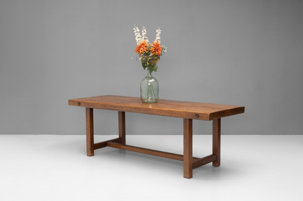 A long rustic wooden farmhouse dining table with a thick plank top, square legs, and an H-stretcher base.