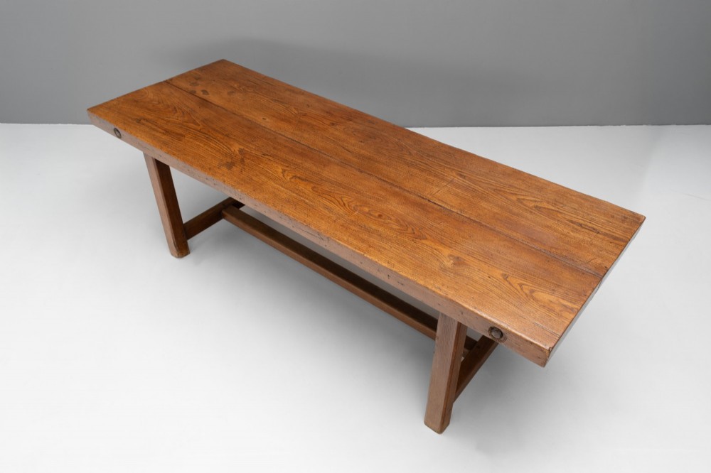 A long rustic wooden farmhouse dining table with a thick plank top, square legs, and an H-stretcher base. View III