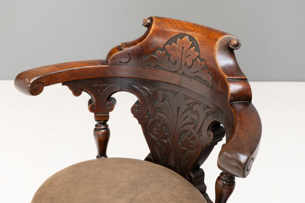 A dark brown Victorian swivel armchair featuring a carved wooden back support and a padded brown leather circular seat. View IV