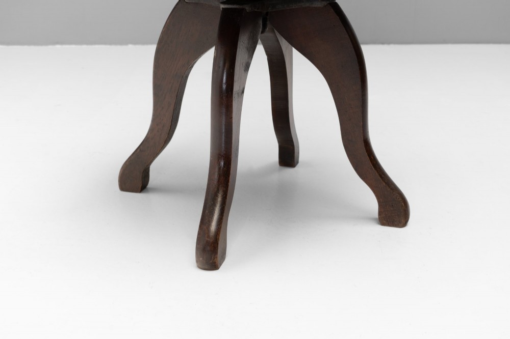 A dark brown Victorian swivel armchair featuring a carved wooden back support and a padded brown leather circular seat. View VI