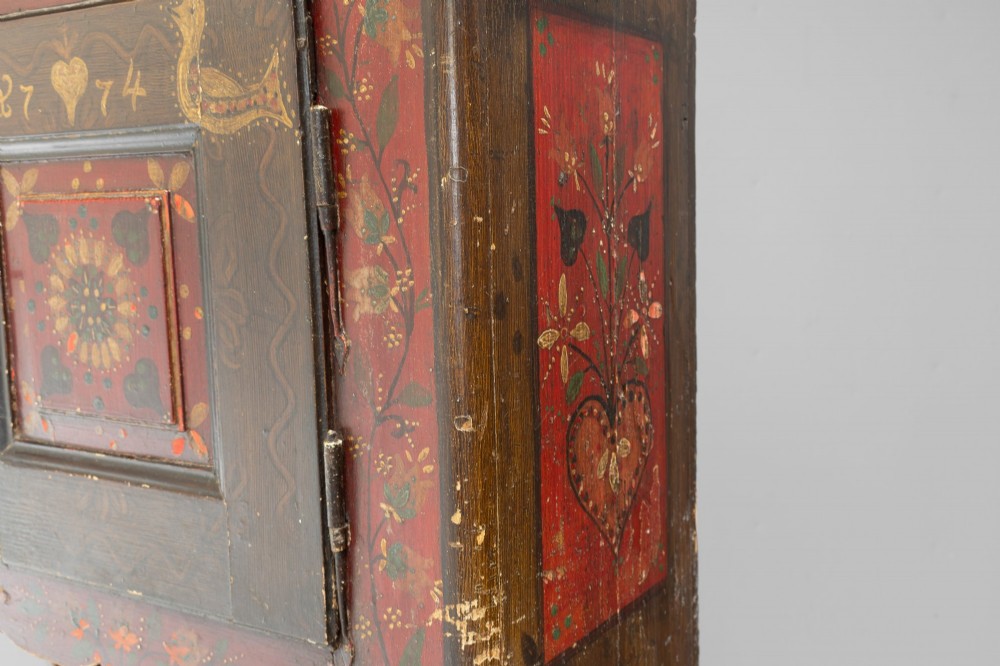 A tall, narrow folk art painted timber cupboard featuring hand-painted floral motifs, date lettering, an upper door, an open central shelf, and a lower door. View IV