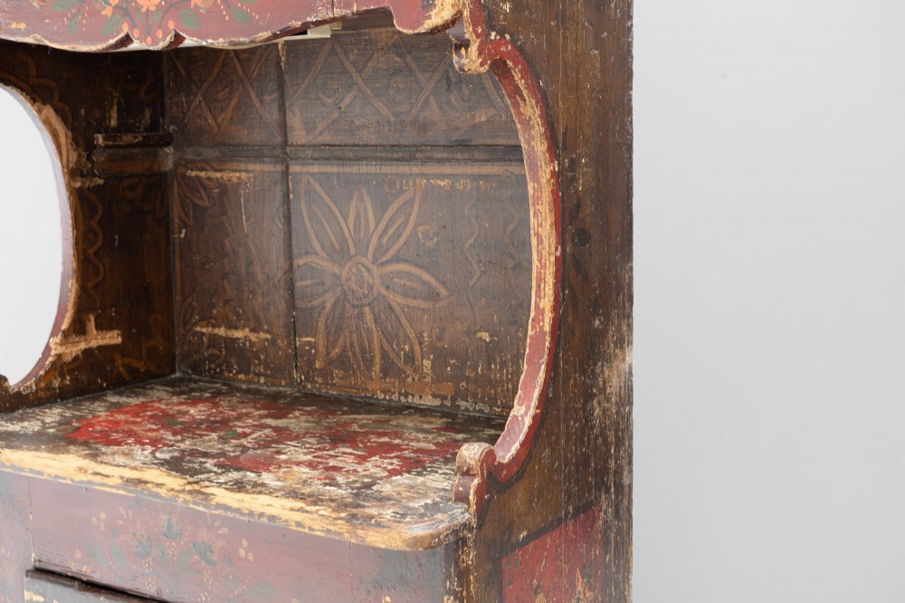 A tall, narrow folk art painted timber cupboard featuring hand-painted floral motifs, date lettering, an upper door, an open central shelf, and a lower door. View V