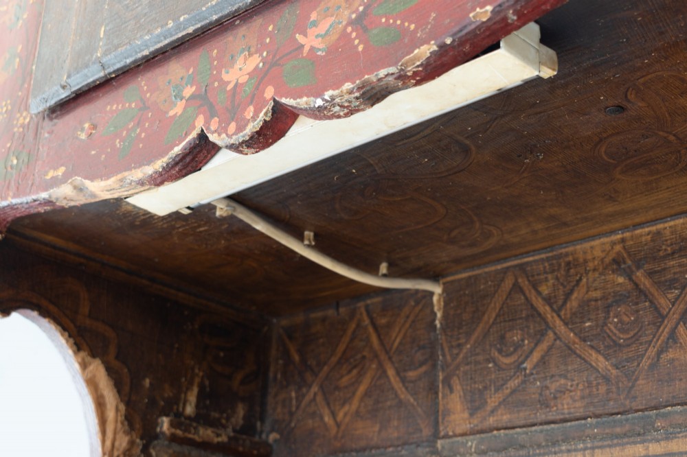 A tall, narrow folk art painted timber cupboard featuring hand-painted floral motifs, date lettering, an upper door, an open central shelf, and a lower door. View X