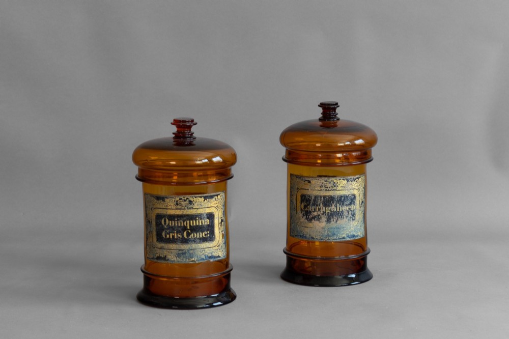 A pair of cylindrical amber glass apothecary jars with glass stoppers and original gilded French labels.