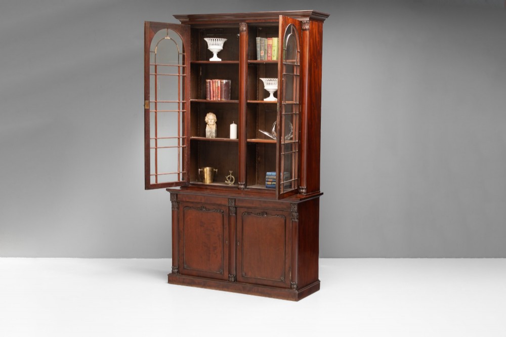 A large mahogany two-tier bookcase featuring twin upper glazed doors with arched glazing bars and a lower cupboard section with carved accents.