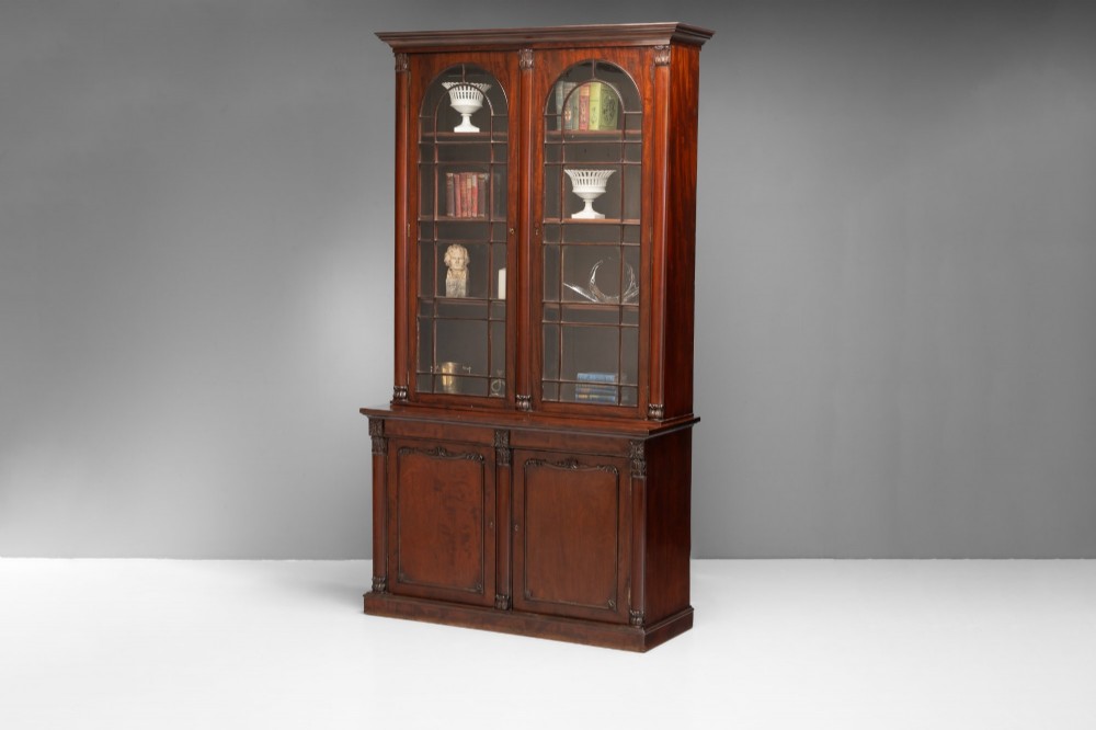 A large mahogany two-tier bookcase featuring twin upper glazed doors with arched glazing bars and a lower cupboard section with carved accents. View IV