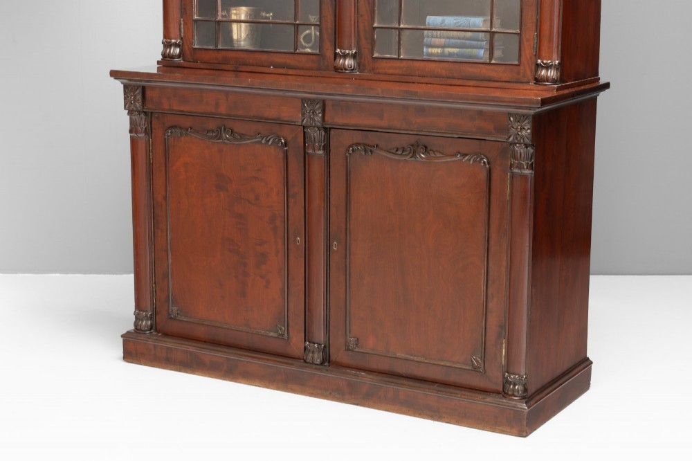 A large mahogany two-tier bookcase featuring twin upper glazed doors with arched glazing bars and a lower cupboard section with carved accents. View V