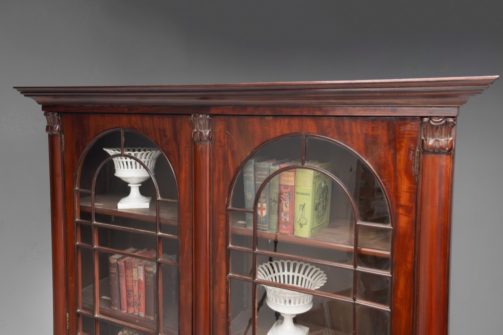 A large mahogany two-tier bookcase featuring twin upper glazed doors with arched glazing bars and a lower cupboard section with carved accents. View XI