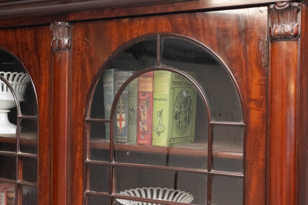 A large mahogany two-tier bookcase featuring twin upper glazed doors with arched glazing bars and a lower cupboard section with carved accents. View XII